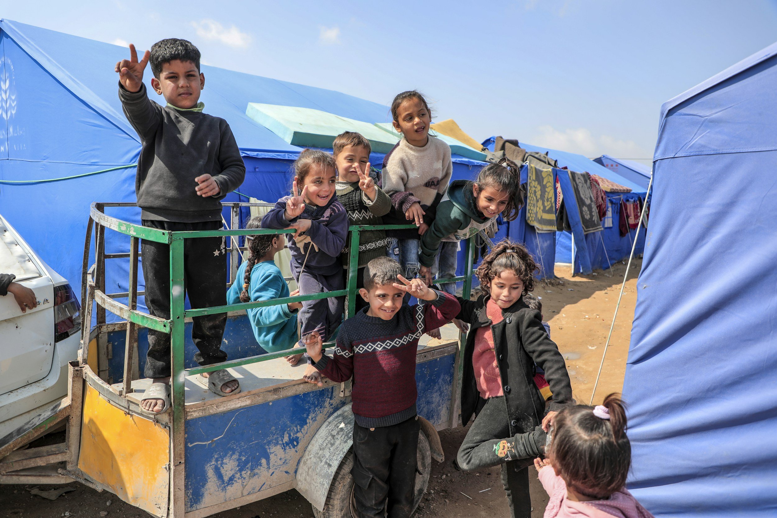 Children in Gaza smiling and waving — the Palestine Children's Relief Fund supports pediatric healthcare in the region.
